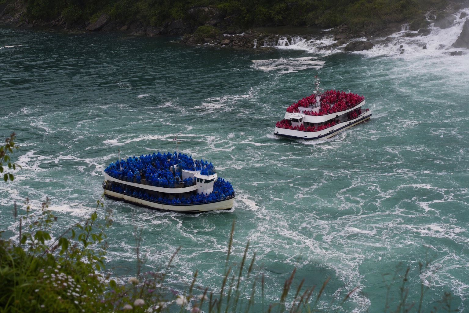 A deck of passengers in blue ponchos passing a deck of passengers in red ponchos in the Niagara gorge