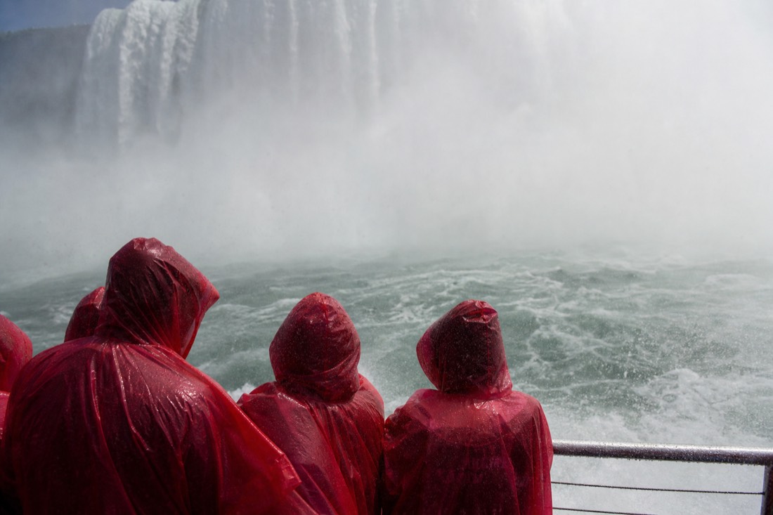 Red-poncho passengers packed along the rail as spray sweeps the deck